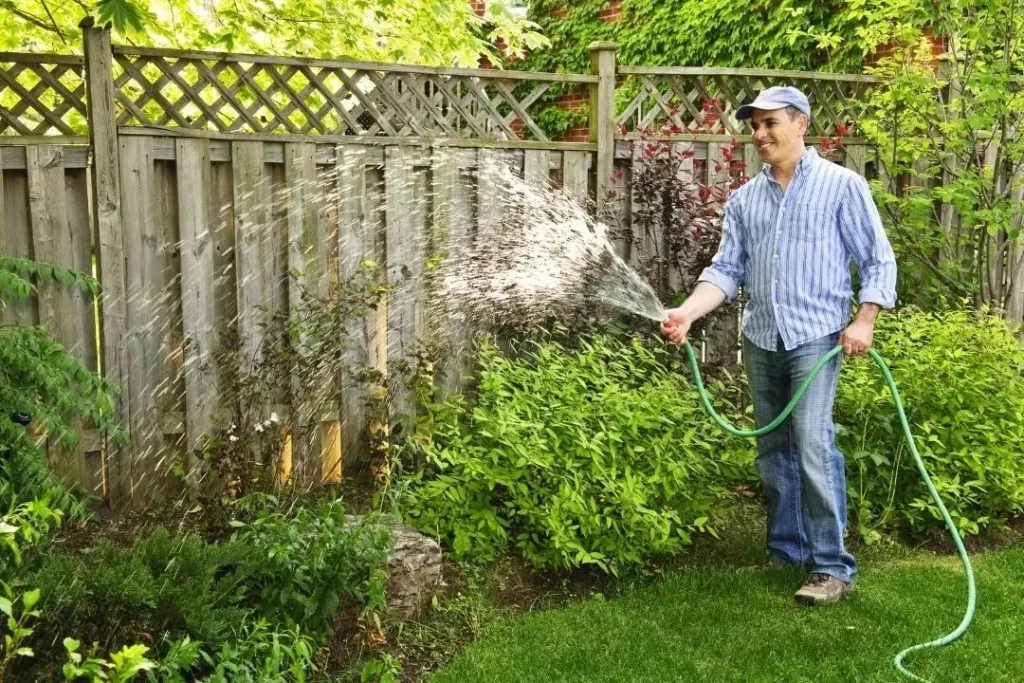 man watering near a fence
